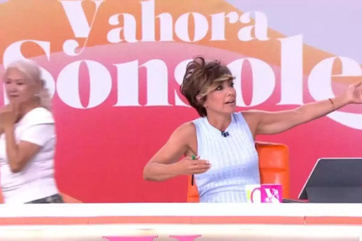 Sonsoles Ónega sentada en un plató de Y ahora Sonsoles gesticulando con los brazos extendidos mientras otra mujer pasa por detrás y el fondo muestra un cartel colorido con letras grandes. Sonsoles Ónega sentada en un plató de Y ahora Sonsoles gesticulando con los brazos extendidos mientras otra mujer pasa por detrás y el fondo muestra un cartel colorido con letras grandes.