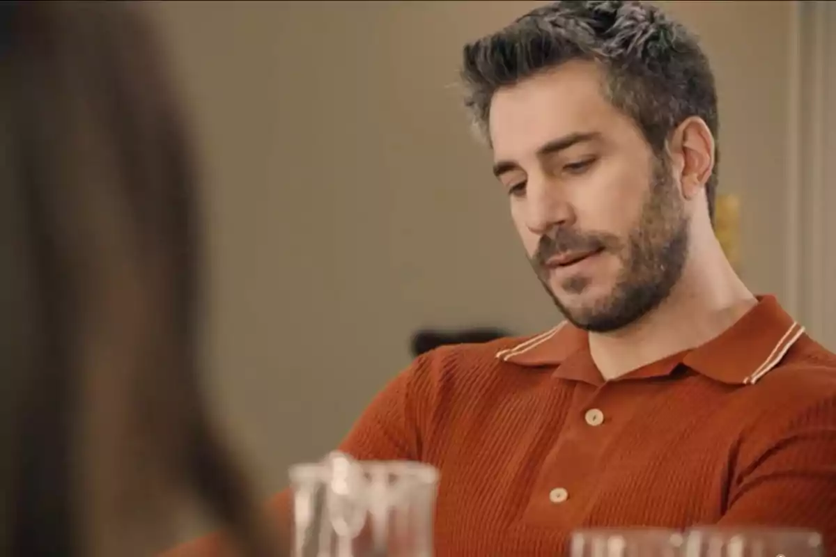 Andrés amb expressió seriosa portant una camisa de polo taronja assegut a una taula. Captura de 'Sueños de libertad' Andrés amb expressió seriosa portant una camisa de polo taronja assegut a una taula. Captura de 'Sueños de libertad'