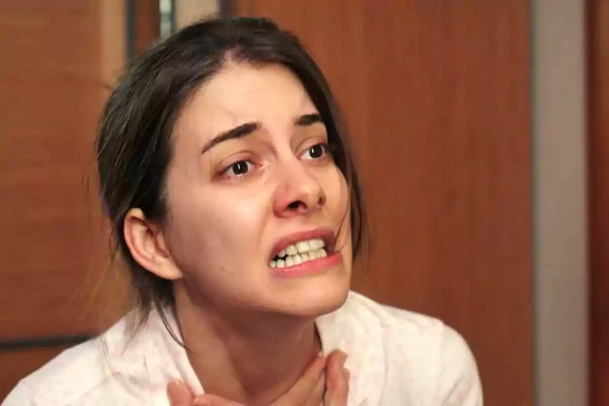 Suna jove amb expressió d’angoixa i les mans al coll en un ambient interior a Una nova vida Suna jove amb expressió d’angoixa i les mans al coll en un ambient interior a Una nova vida