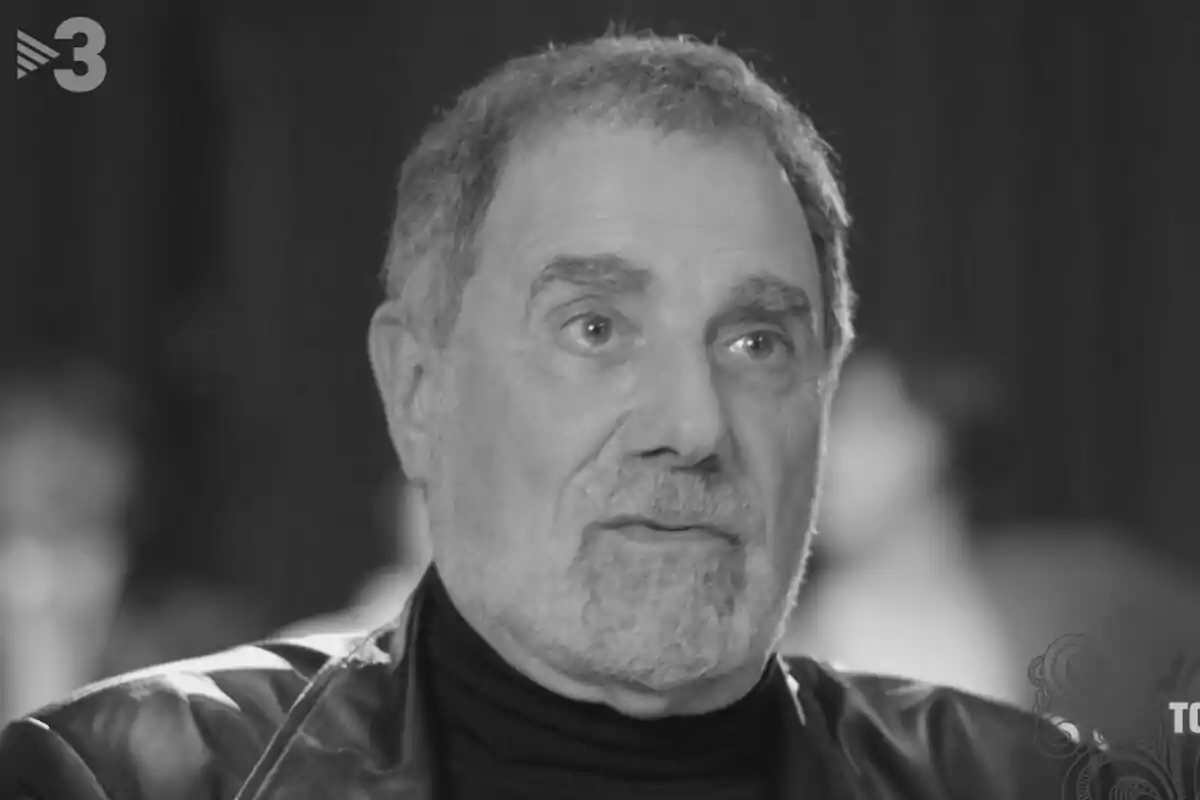 Toni Cruz mayor de cabello canoso y barba corta con chaqueta de cuero y suéter oscuro en una entrevista en blanco y negro