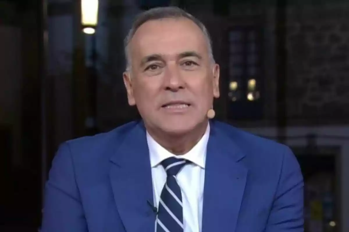 Xabier Fortes, d’edat mitjana, amb cabell curt i canós, porta un vestit blau i una corbata de ratlles mentre utilitza un micròfon de diadema a La Nit a 24 Hores.