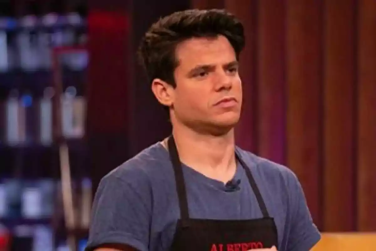 Alberto Gras joven con cabello oscuro y camiseta azul usando un mandil negro en un set de cocina de MasterChef