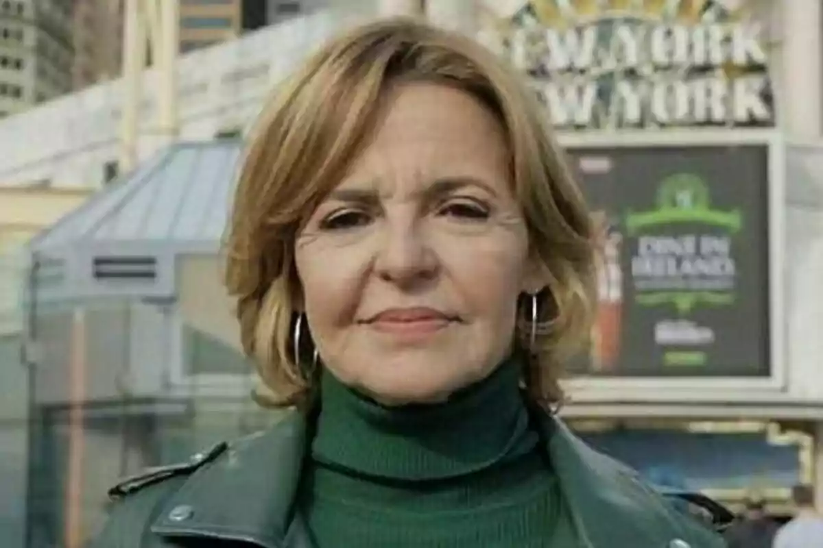 Almudena Ariza de cabello corto rubio con chaqueta y suéter verde posando al aire libre frente a un letrero que dice New York