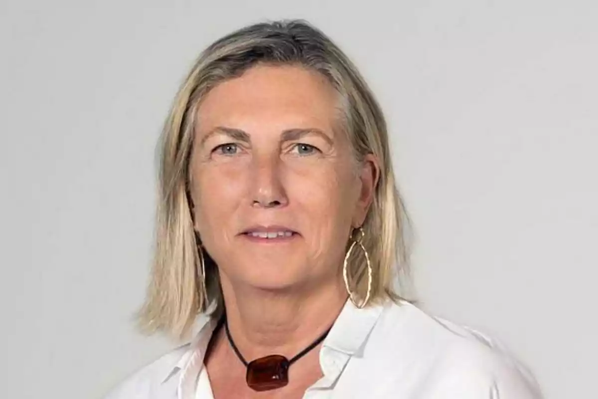 Ana María Bordas de cabell ros i curt amb camisa blanca, collaret fosc i arracada daurada, posant davant d’un fons gris clar