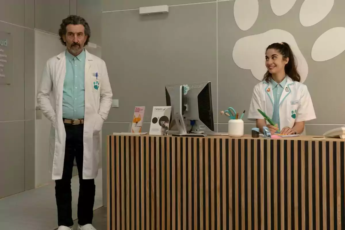 Luis Zahera i Lucía Caraballo, com a veterinaris amb bata blanca, són a la recepció d’una clínica veterinària moderna; un està dret i l’altra asseguda somrient darrere del taulell a la sèrie Animal. Luis Zahera i Lucía Caraballo, com a veterinaris amb bata blanca, són a la recepció d’una clínica veterinària moderna; un està dret i l’altra asseguda somrient darrere del taulell a la sèrie Animal.