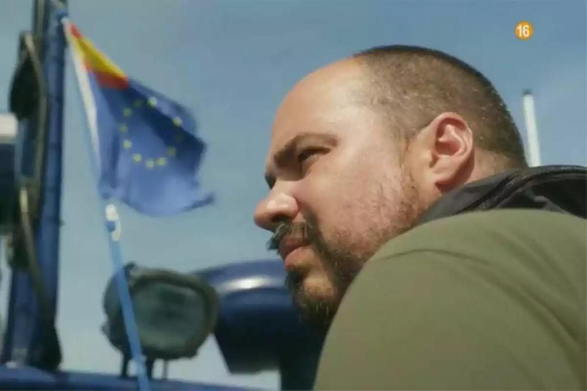 Antonio Pampliega de perfil mirando hacia el horizonte con una bandera de la Unión Europea ondeando al fondo en un día soleado en Territorio Pampliega Antonio Pampliega de perfil mirando hacia el horizonte con una bandera de la Unión Europea ondeando al fondo en un día soleado en Territorio Pampliega