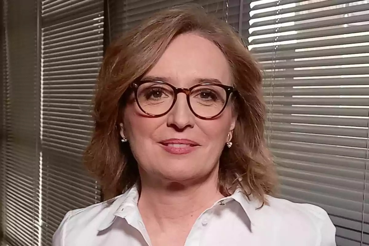 Beatriz Ariño de cabello castaño claro y gafas, con camisa blanca, posando frente a una ventana con persianas.