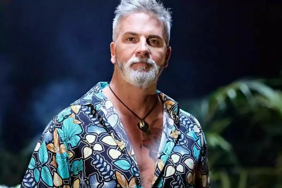 Carlos Alba de cabell i barba canosos amb camisa colorida d’estampat floral i fons fosc amb plantes desenfocades a Supervivientes All Stars Carlos Alba de cabell i barba canosos amb camisa colorida d’estampat floral i fons fosc amb plantes desenfocades a Supervivientes All Stars