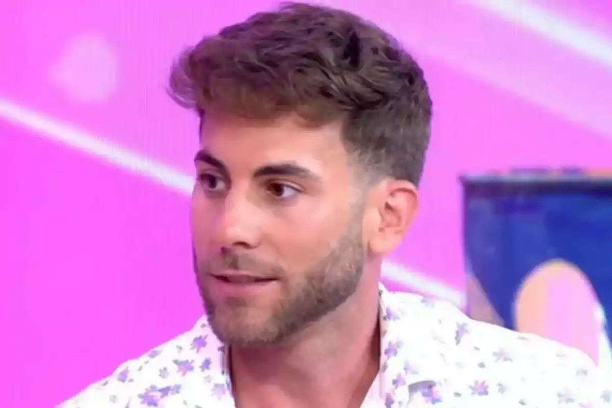 César Muñoz joven con barba y cabello corto, vistiendo una camisa blanca con estampado de flores, en un set de televisión con fondo rosa en Fiesta. César Muñoz joven con barba y cabello corto, vistiendo una camisa blanca con estampado de flores, en un set de televisión con fondo rosa en Fiesta.