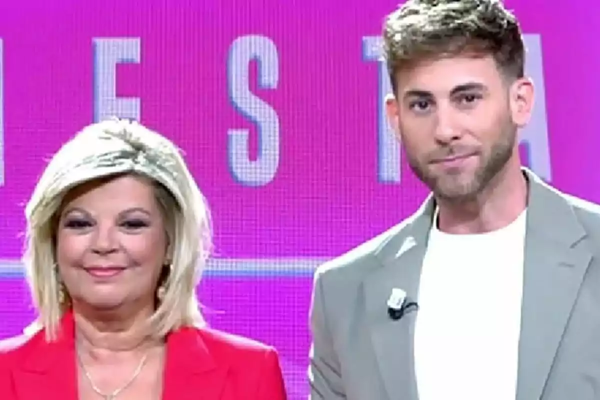Terelu Campos i César Muñoz a Fiesta posen somrients davant d’un fons rosa amb lletres grans.