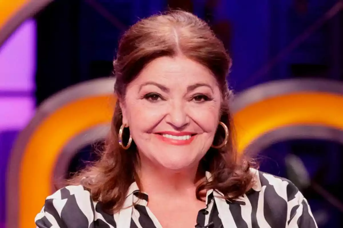 Charo Reina de cabello castaño sonriente con blusa de rayas blancas y negras y aretes grandes en un set iluminado de MasterChef Celebrity