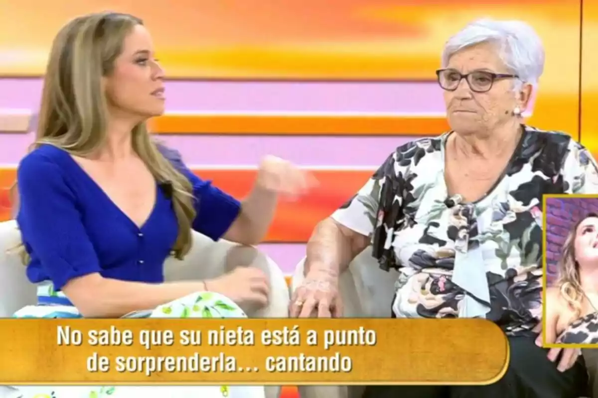Dos mujeres sentadas en un set de televisión colorido de El Diario de Jorge, Cristina Lasvignes con cabello largo y rubio viste un suéter azul y la otra es una señora mayor con gafas y cabello canoso, ambas conversan mientras en la pantalla aparece un recuadro con el rostro de una joven y un texto que dice que la nieta está a punto de sorprender a su abuela cantando. Dos mujeres sentadas en un set de televisión colorido de El Diario de Jorge, Cristina Lasvignes con cabello largo y rubio viste un suéter azul y la otra es una señora mayor con gafas y cabello canoso, ambas conversan mientras en la pantalla aparece un recuadro con el rostro de una joven y un texto que dice que la nieta está a punto de sorprender a su abuela cantando.