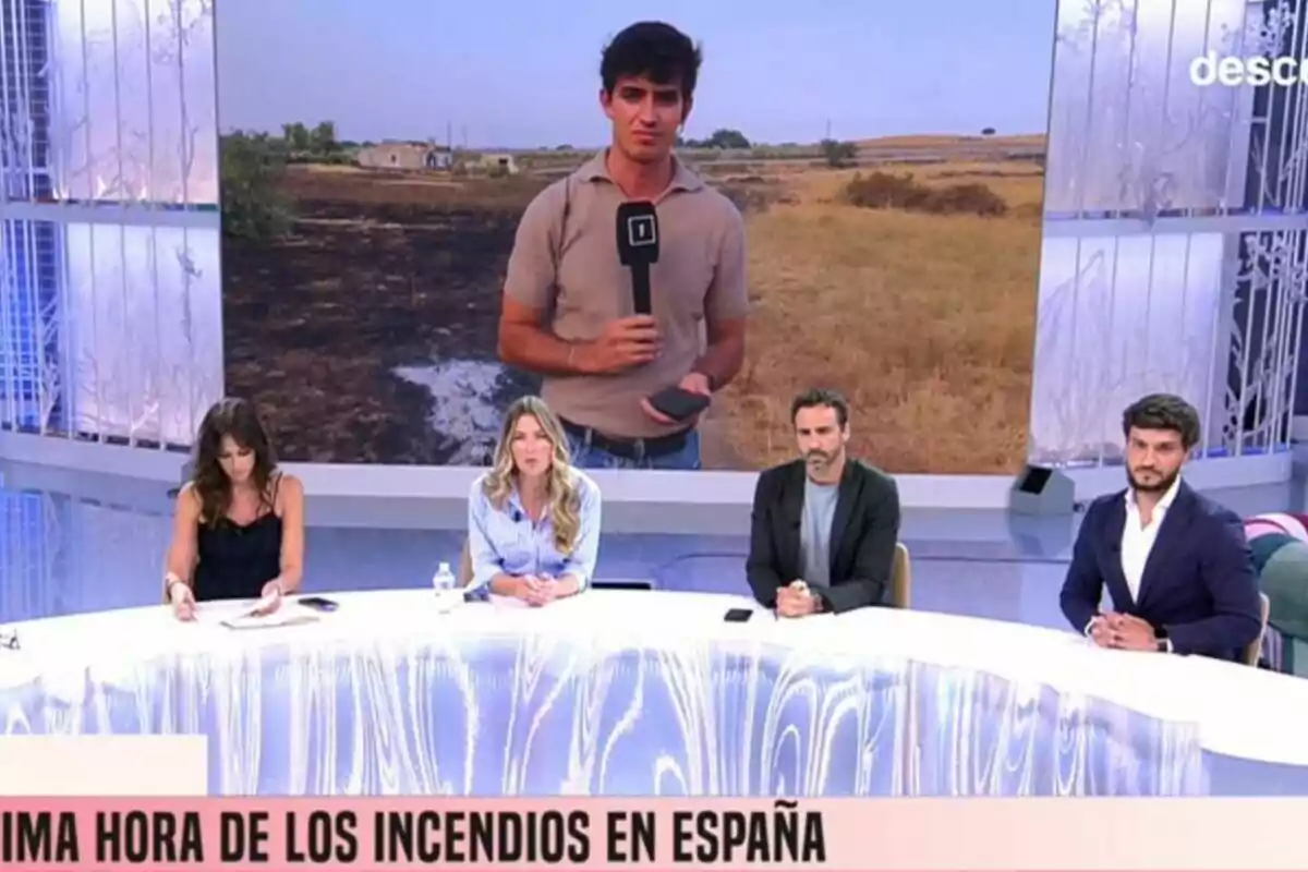 Àlex Blanquer juntament amb tres col·laboradors estan asseguts en una taula de Festa mentre en una pantalla gran apareix un reporter a l’exterior informant sobre incendis a Espanya. Àlex Blanquer juntament amb tres col·laboradors estan asseguts en una taula de Festa mentre en una pantalla gran apareix un reporter a l’exterior informant sobre incendis a Espanya.