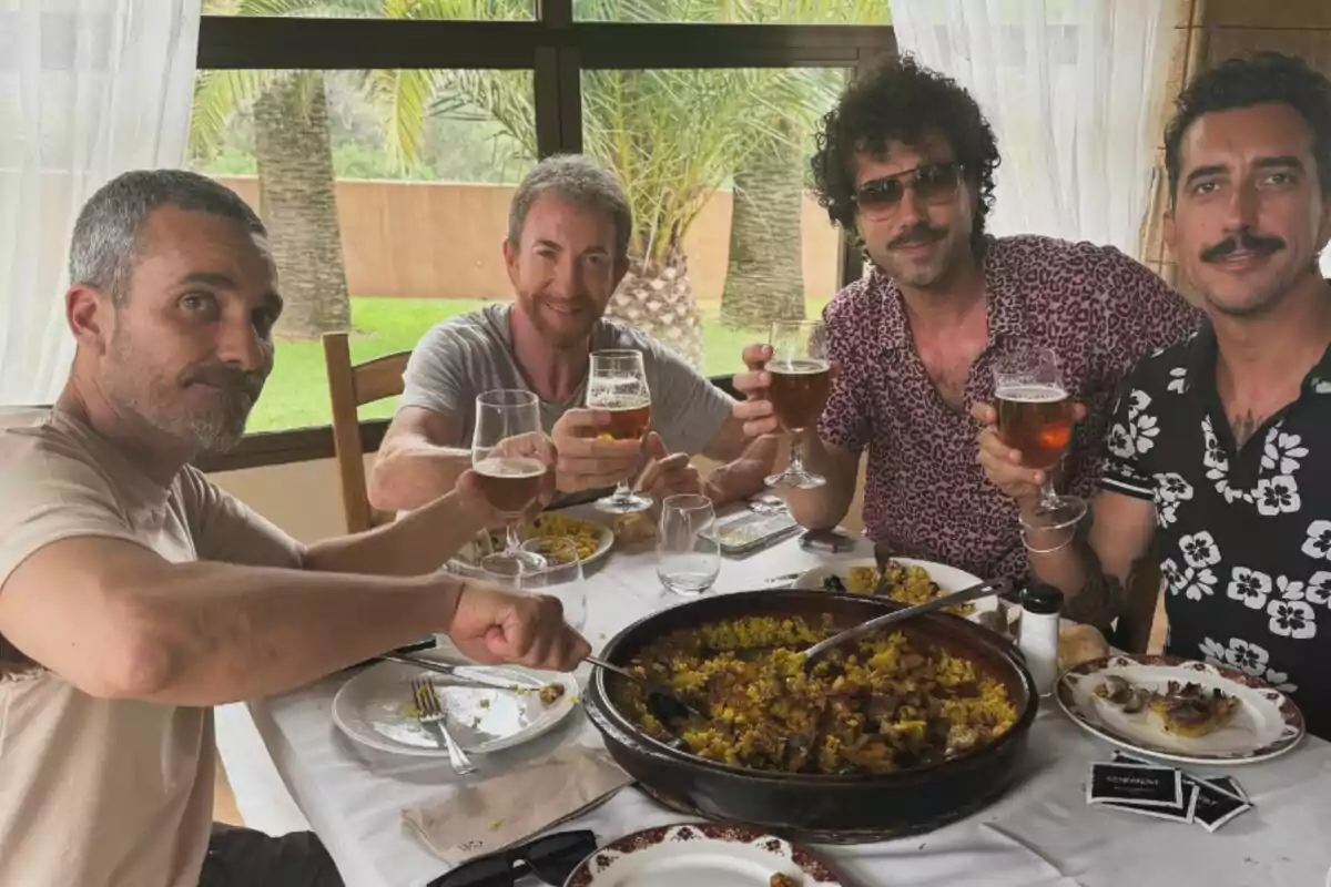 Pablo Motos, Damián Mollá, Juan Ibañez i Marron brinden amb copes de cervesa mentre gaudeixen d’un àpat junts en una taula amb un gran plat d’arròs, en un ambient lluminós amb vista a un jardí. Pablo Motos, Damián Mollá, Juan Ibañez i Marron brinden amb copes de cervesa mentre gaudeixen d’un àpat junts en una taula amb un gran plat d’arròs, en un ambient lluminós amb vista a un jardí.