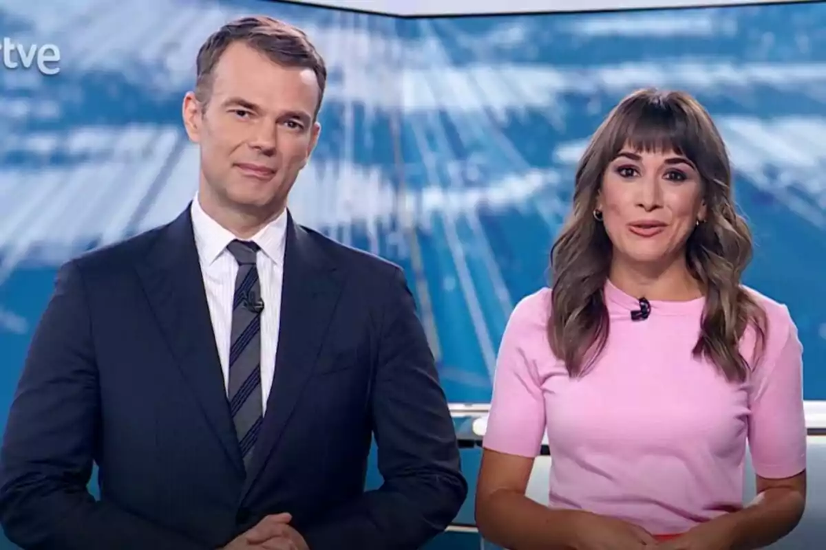Igor Gómez y Marina Ribel de noticias están de pie en un estudio del Telediario, el hombre lleva traje oscuro y corbata mientras que la mujer viste una camiseta rosa, ambos miran a la cámara y sonríen.