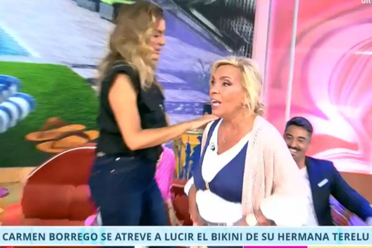 Dues dones interactuen en un plató de televisió colorit mentre un home somriu al fons i a la part inferior apareix un text que esmenta a Carmen Borrego i un biquini.