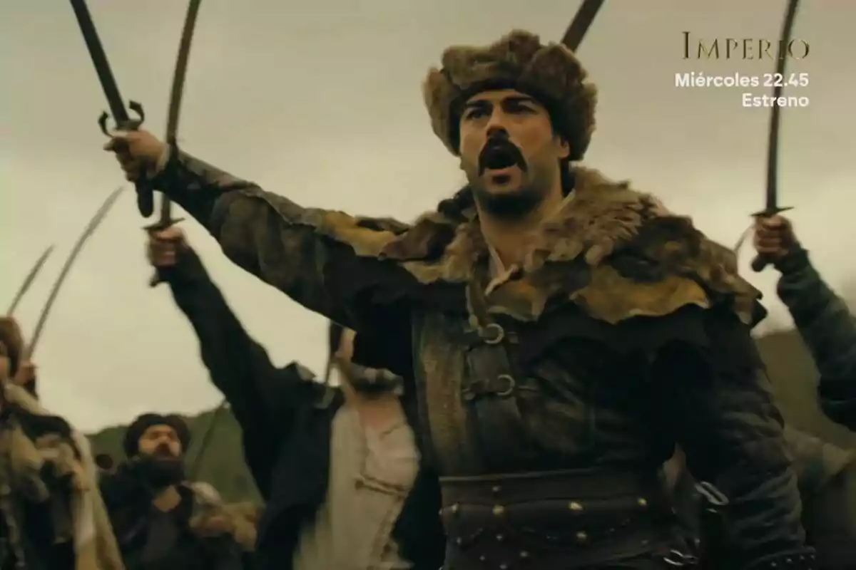 Home amb vestimenta d’època i barret de pell liderant un grup de guerrers que alcen espases enlaire a l’Imperi Home amb vestimenta d’època i barret de pell liderant un grup de guerrers que alcen espases enlaire a l’Imperi