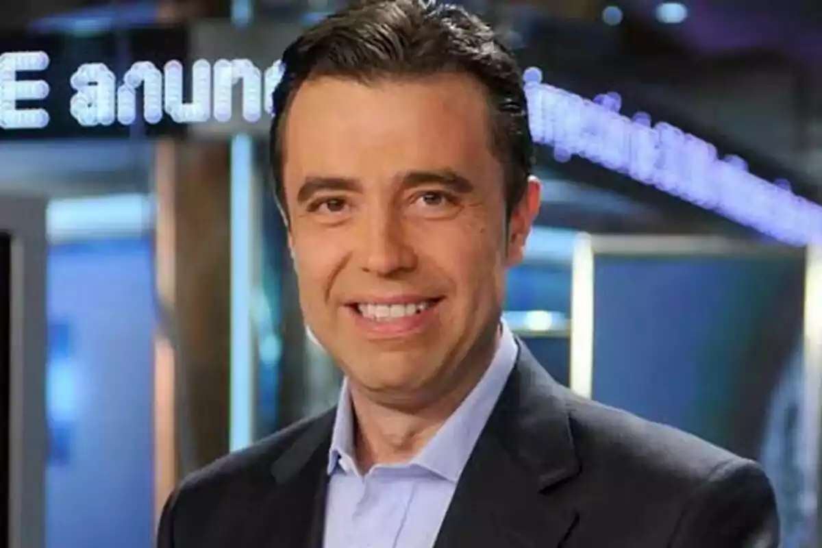 José Antonio Luque de cabello oscuro con traje y camisa clara sonriendo en un estudio de televisión de Informativos Telecinco con luces y pantallas al fondo