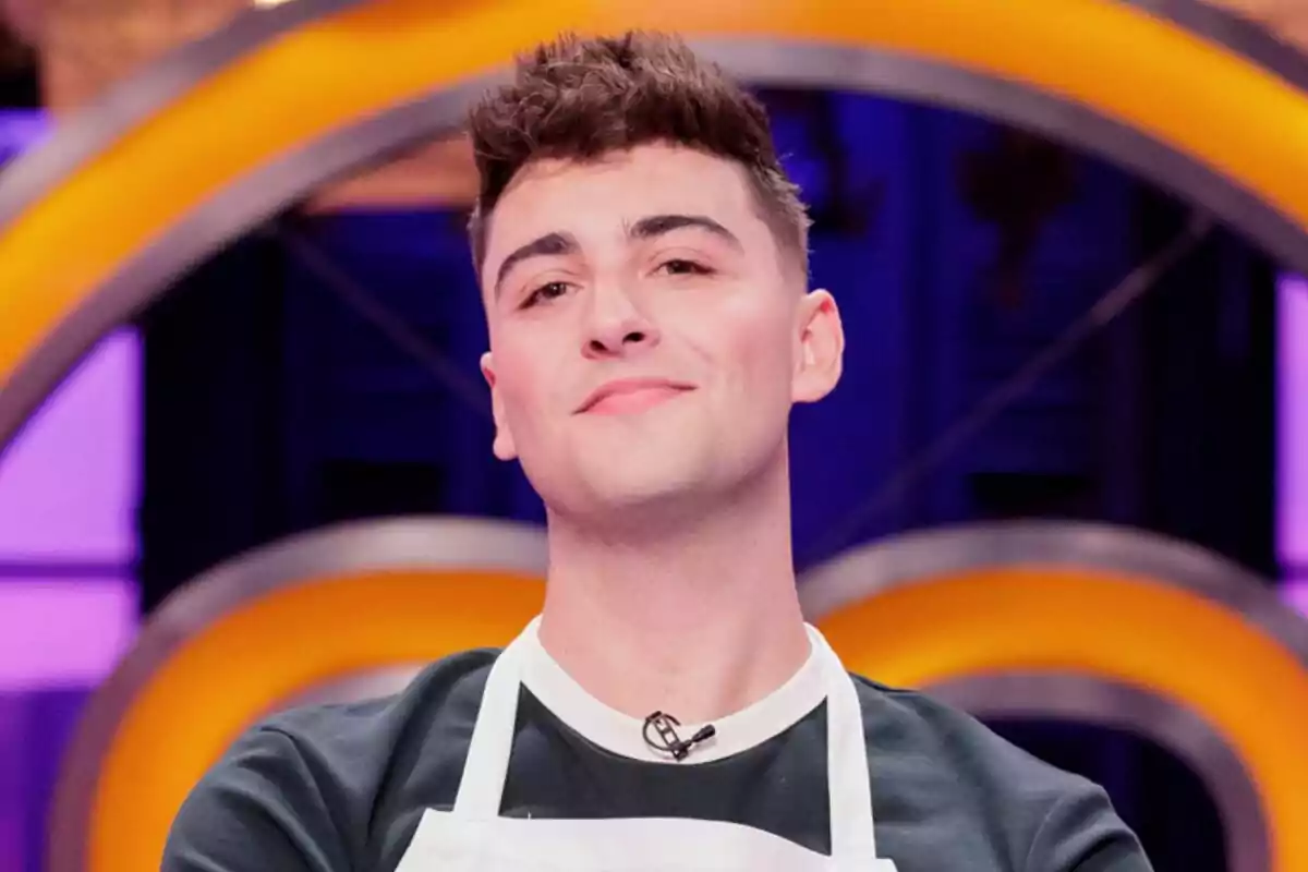 Posat de Juanjo Bona somrient mentre mira a càmera amb el davantal de MasterChef Celebrity i un fons acolorit