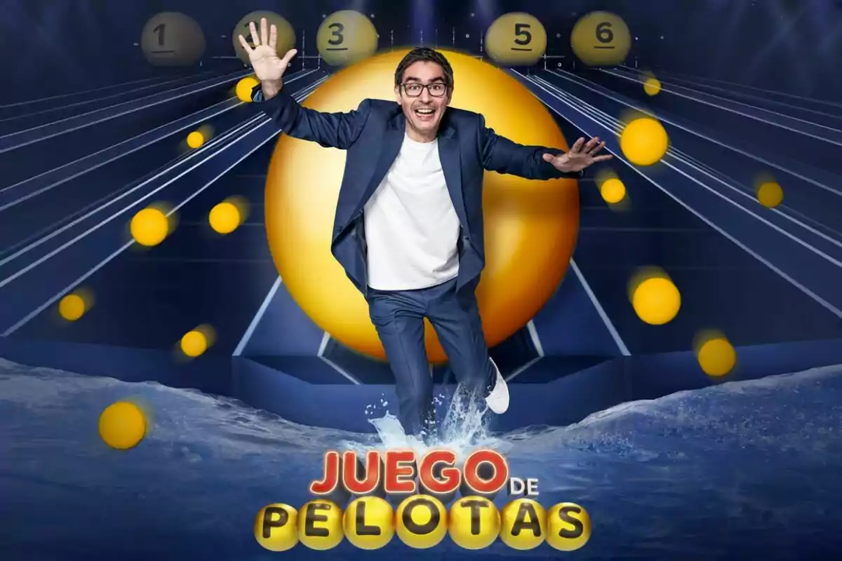 Juanra Bonet somrient amb ulleres i vestit blau salta davant d’una gran pilota groga envoltat d’esferes grogues i el text Joc de Pilotes a la part inferior Juanra Bonet somrient amb ulleres i vestit blau salta davant d’una gran pilota groga envoltat d’esferes grogues i el text Joc de Pilotes a la part inferior
