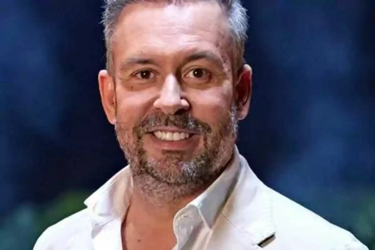 Kike Calleja de cabell curt i canós amb barba i bigoti, somrient, vestit amb americana clara i camisa blanca, fons fosc desenfocat a Supervivientes All Stars