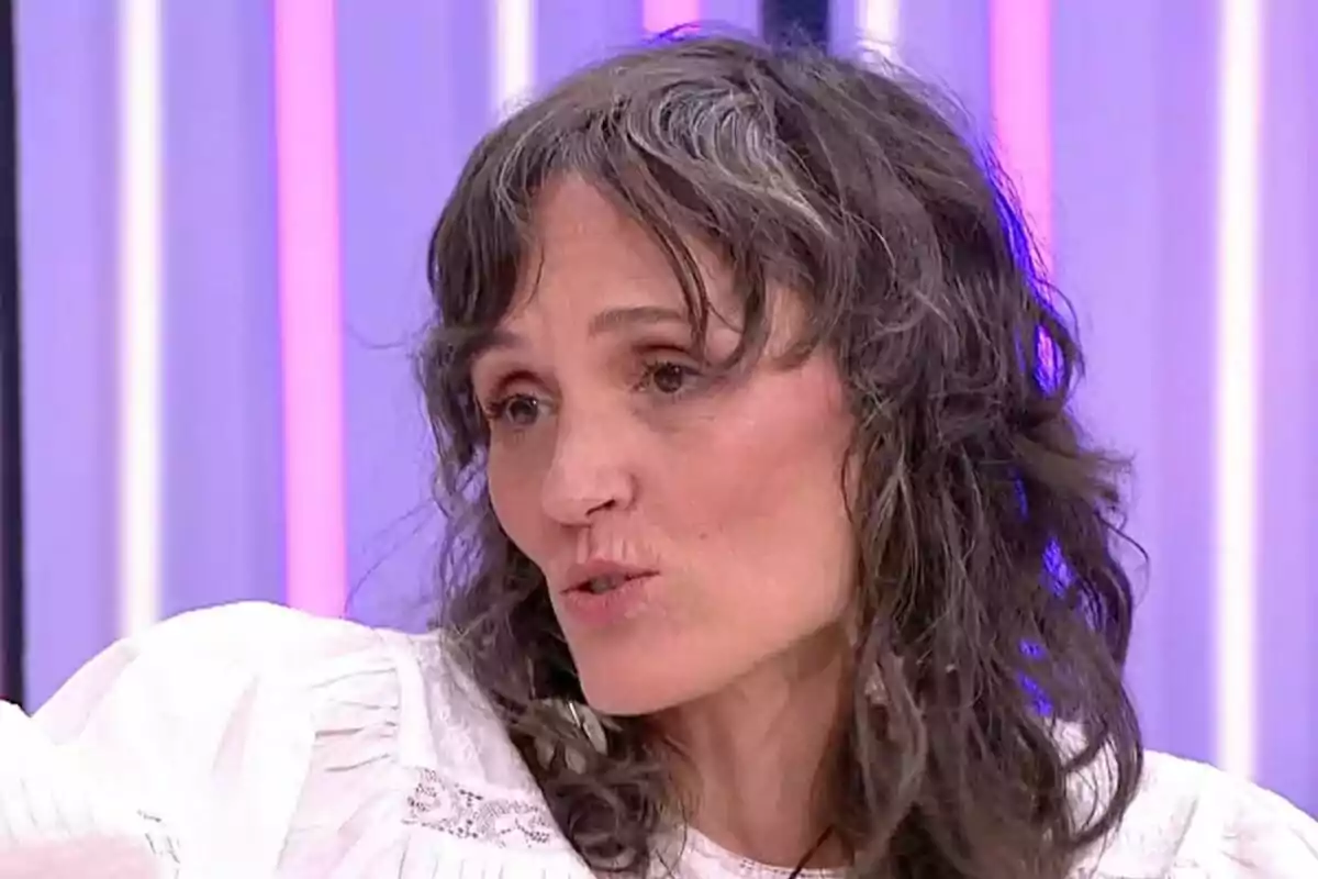 Laura Pamplona de cabello ondulado y canoso con blusa blanca hablando en un set de Y ahora Sonsoles con luces de colores en el fondo