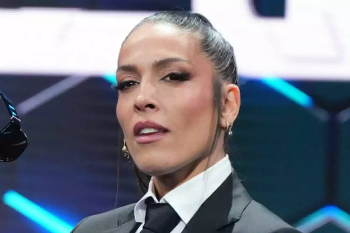 Lorena Castell amb els cabells recollits vestida amb vestit formal i corbata negra en un escenari il·luminat a Caiga quien caiga