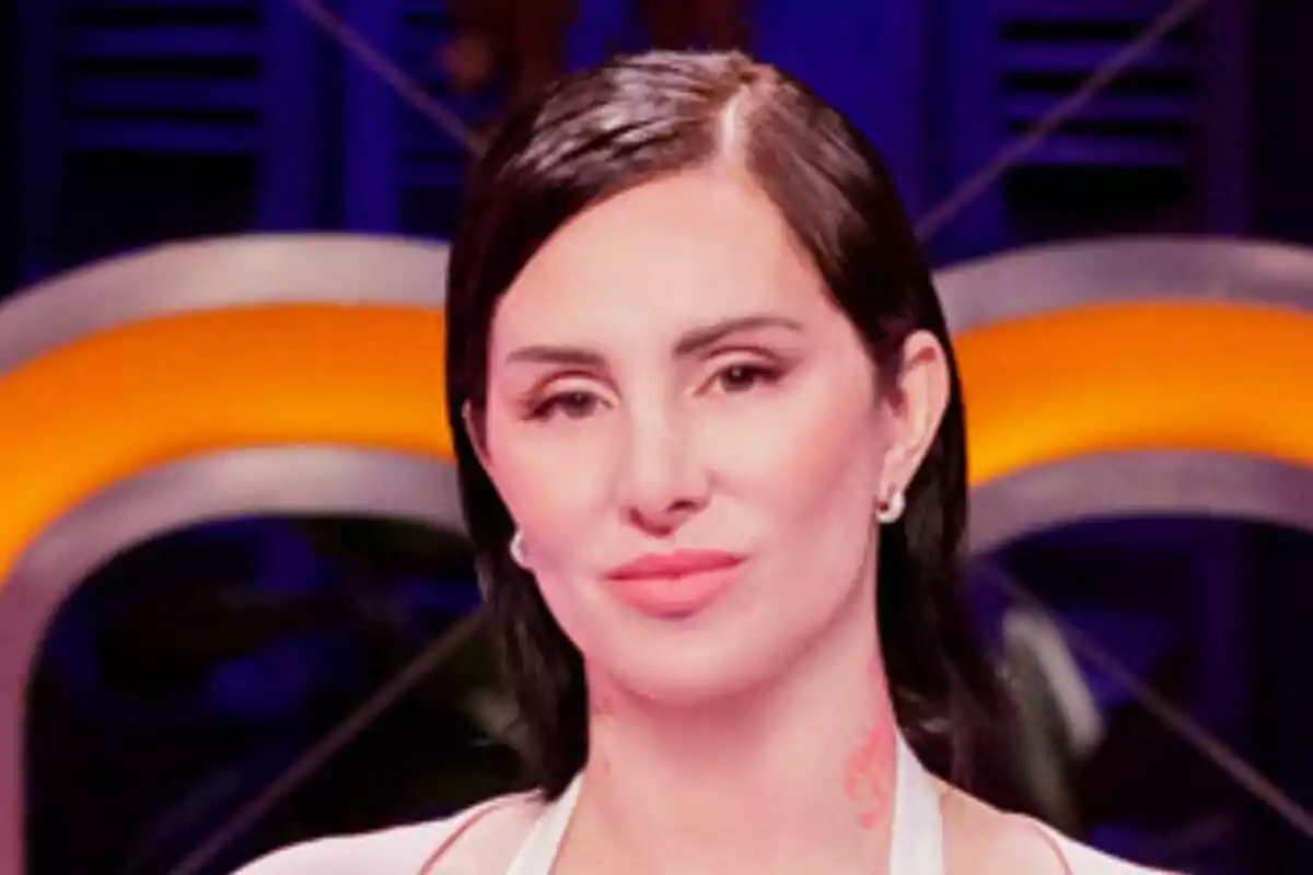 Mala Rodríguez de cabello oscuro y liso con expresión seria, usando aretes pequeños y fondo desenfocado con luces naranjas y azules de MasterChef Celebrity