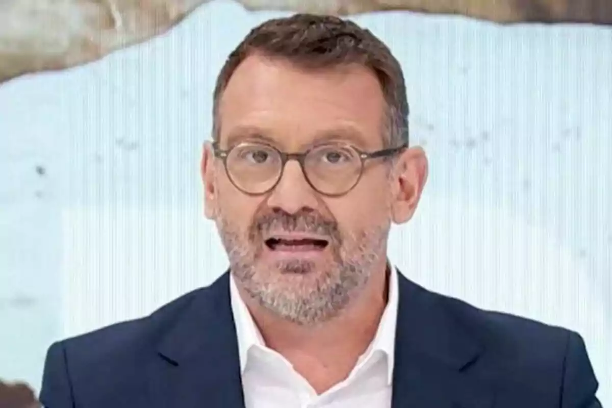 Marc Sala de mitjana edat amb ulleres i barba, vestit amb americana blava i camisa blanca, parlant davant d’un fons clar a La Hora de La 1