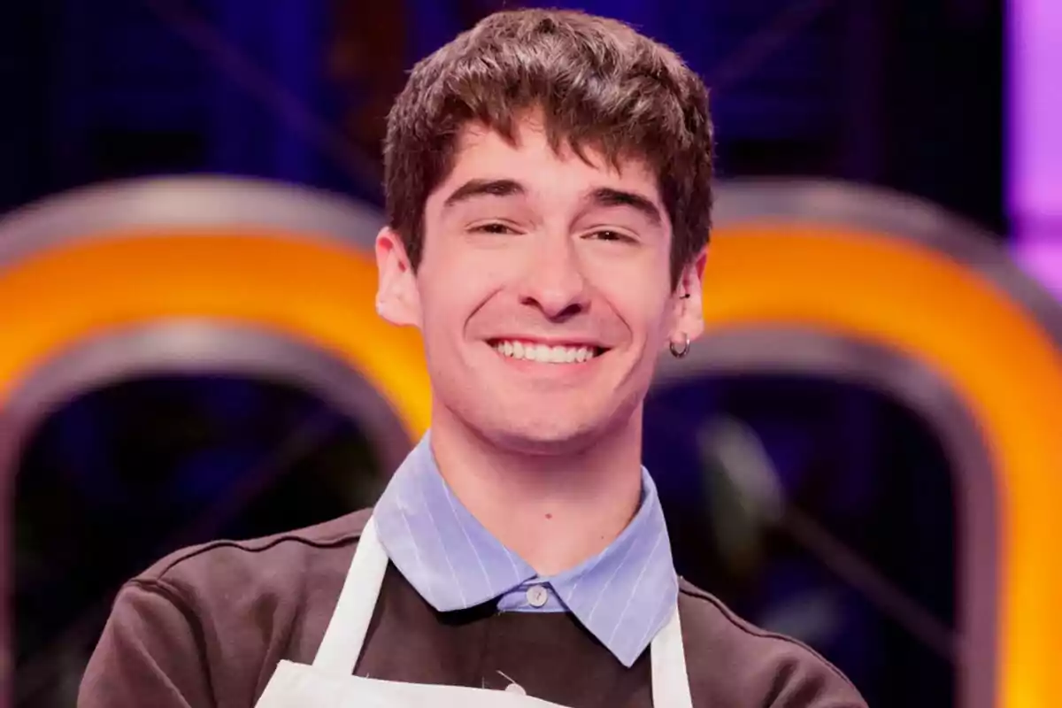 Necho Vidal sonriente con delantal blanco de MasterChef Celebrity y fondo colorido