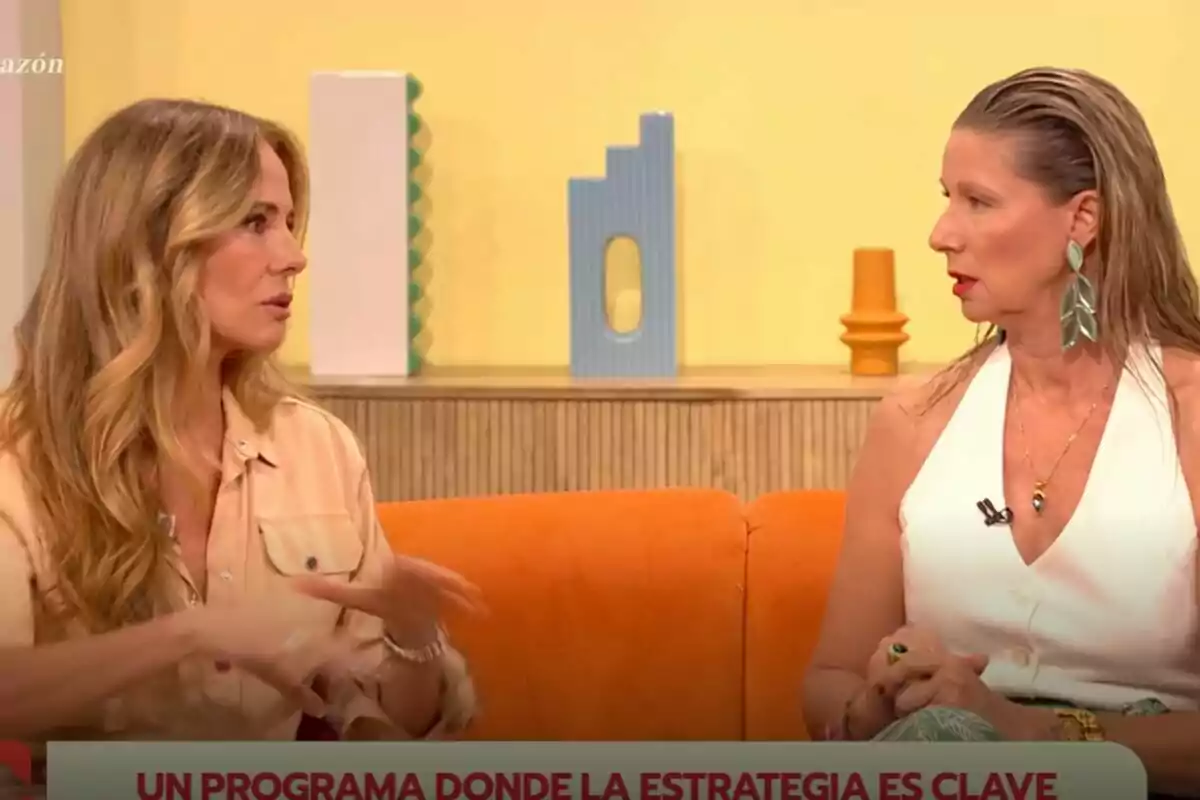 Paula Vázquez i Anne Igartiburu conversen assegudes en un sofà taronja en un plató de D Corazón amb decoració moderna i fons groc. Paula Vázquez i Anne Igartiburu conversen assegudes en un sofà taronja en un plató de D Corazón amb decoració moderna i fons groc.