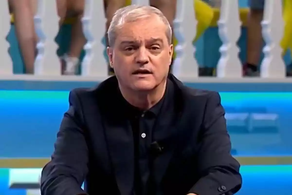 Ramón García de cabell canós i expressió seriosa assegut en un plató de televisió amb fons blau i baranes blanques a El Grand Prix