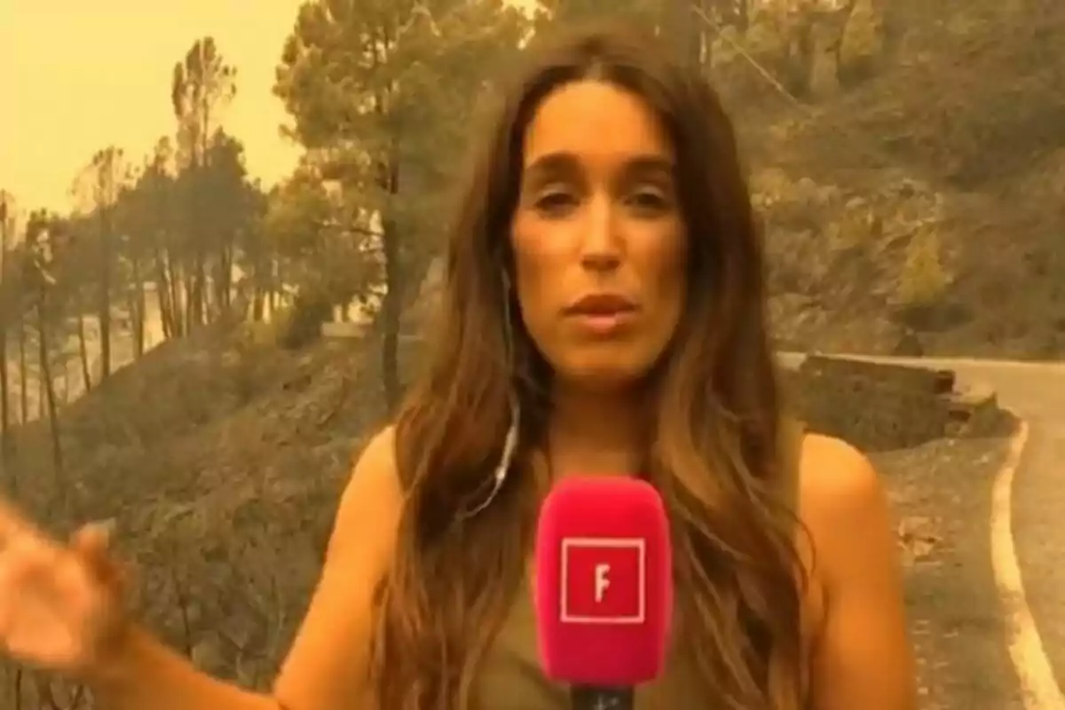 Reportera Arabella Otero amb micròfon rosa de Festa informant des d’una zona boscosa afectada per fum i cendra