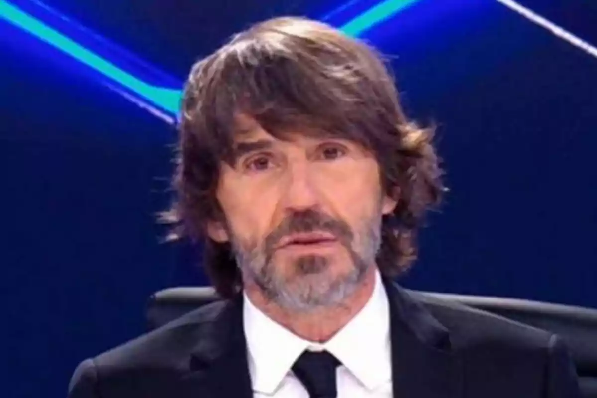 Santi Millán de cabello castaño y barba con traje y corbata en un estudio de Caiga quien caiga con fondo azul