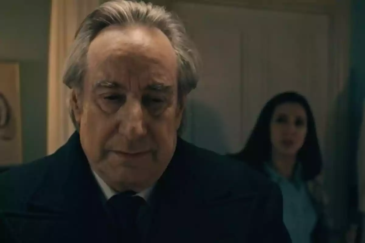 Don Pedro expresión seria está en primer plano mientras una mujer de cabello oscuro aparece desenfocada al fondo en una habitación con luz tenue. Captura de 'Sueños de libertad' Don Pedro expresión seria está en primer plano mientras una mujer de cabello oscuro aparece desenfocada al fondo en una habitación con luz tenue. Captura de 'Sueños de libertad'