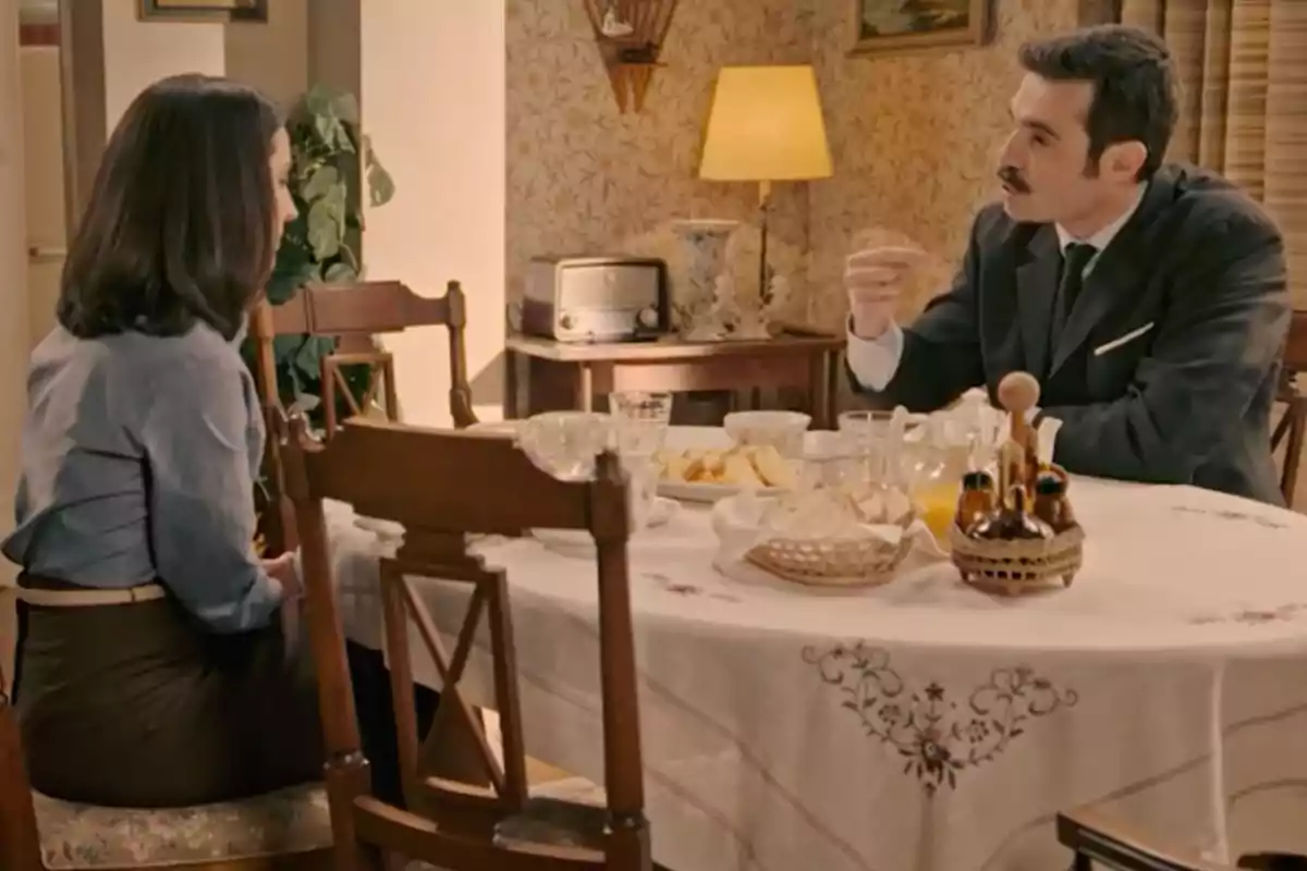 Joaquín i Luz asseguts en una taula rodona coberta amb un mantel blanc decorat, conversant en un menjador amb decoració d’estil antic i menjar sobre la taula. Captura de 'Sueños de libertad' Joaquín i Luz asseguts en una taula rodona coberta amb un mantel blanc decorat, conversant en un menjador amb decoració d’estil antic i menjar sobre la taula. Captura de 'Sueños de libertad'