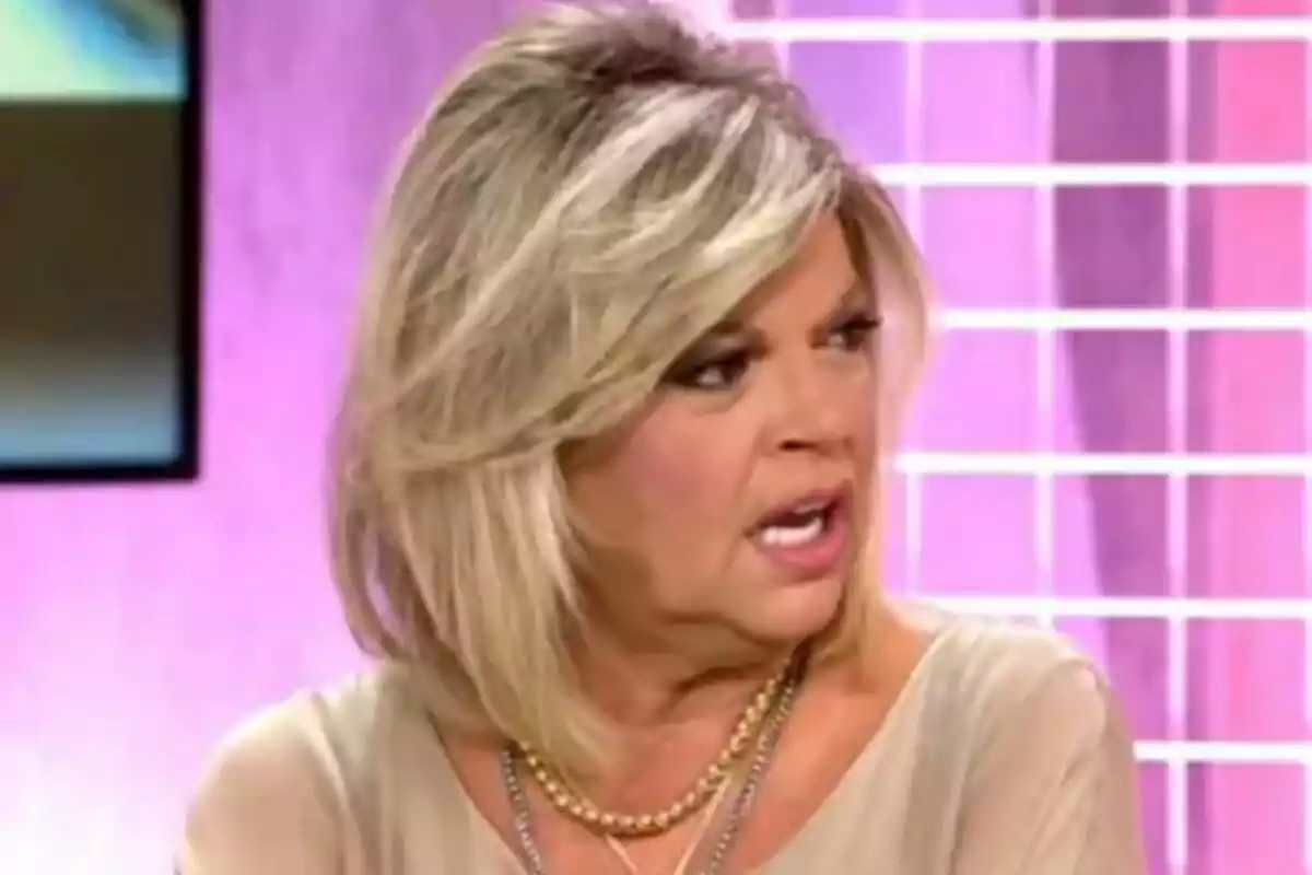 Terelu Campos rossa amb expressió seriosa en un plató de televisió amb fons rosa i reixa blanca a Fiesta