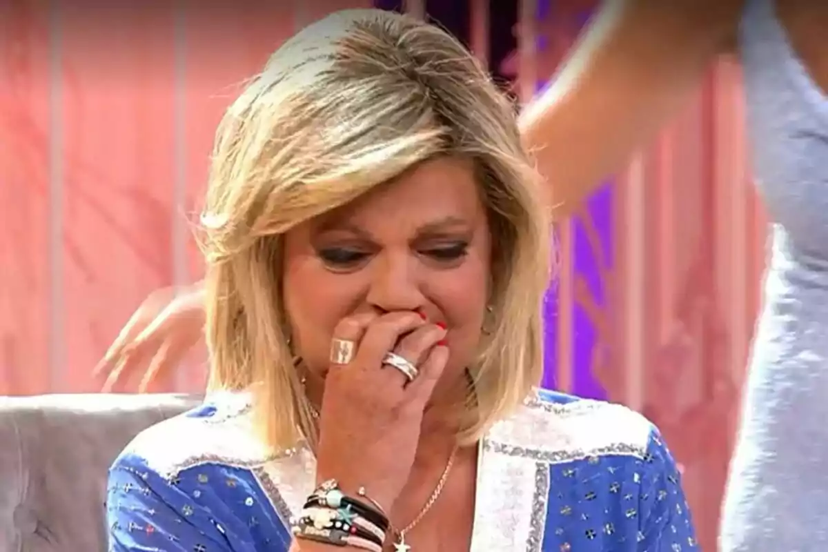 Terelu Campos rubia con expresión de tristeza cubriéndose la boca con la mano en un set de Fiesta