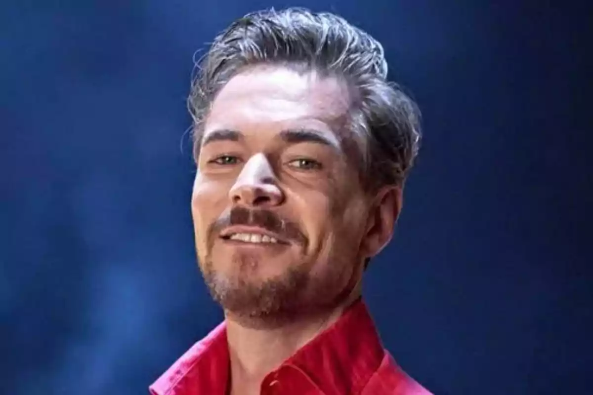 Tony Spina de cabell curt i barba lleugera amb camisa vermella somrient davant d’un fons blau de Supervivientes All Stars.