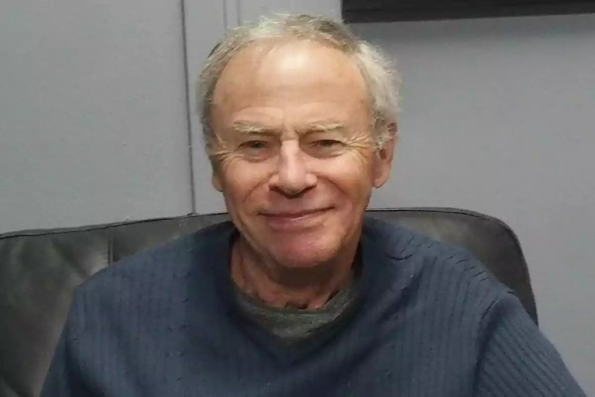Tristan Rogers, més gran, de cabell canós i jersei blau, somrient mentre està assegut en un sofà negre. Tristan Rogers, més gran, de cabell canós i jersei blau, somrient mentre està assegut en un sofà negre.