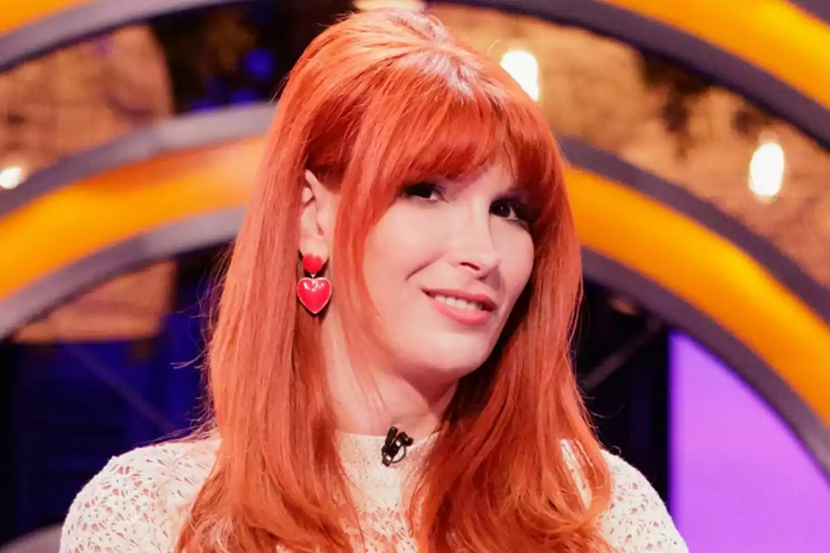 Valeria Vegas pelirroja con cabello largo y flequillo usando pendientes de corazón rojo y blusa clara en un set de MasterChef Celebrity colorido