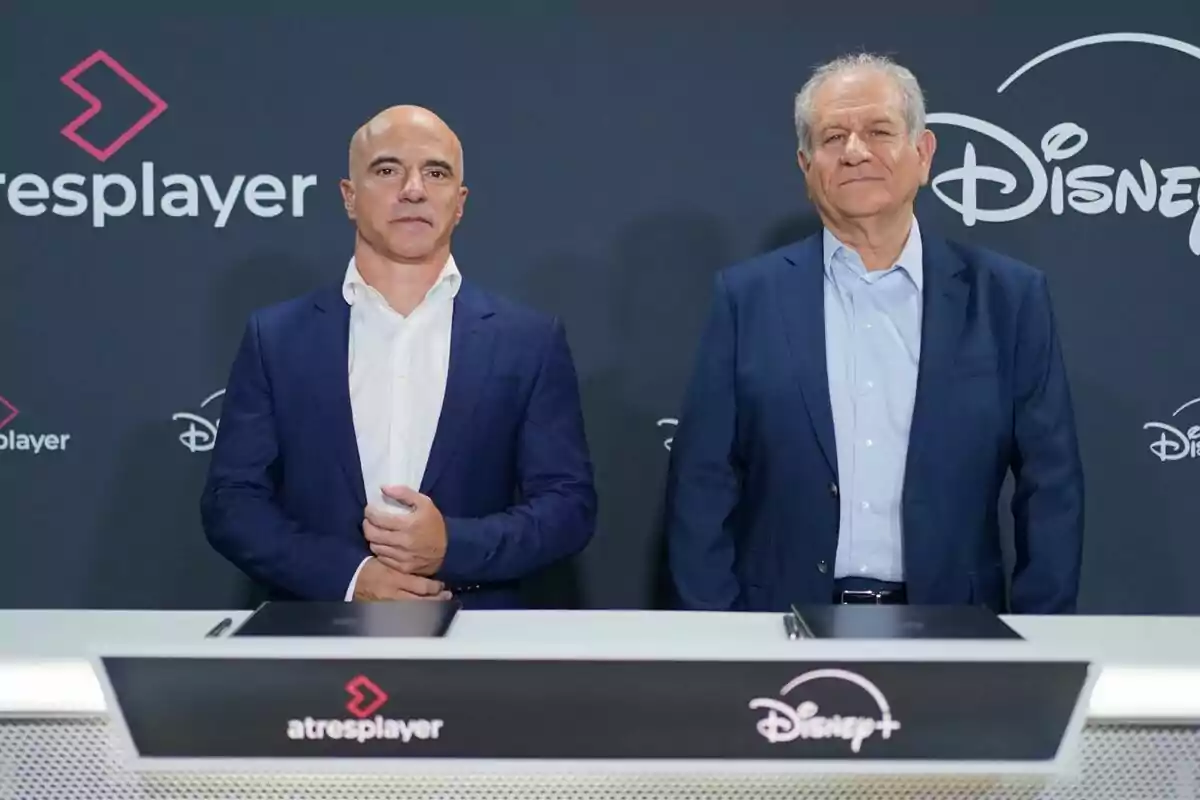 José Antonio Antón y Simon Amselem con traje posan frente a un fondo con los logotipos de atresplayer y Disney Plus durante un evento o firma de acuerdo