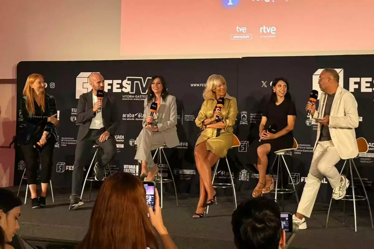 Sis persones com Gonzalo Miró, Marta Flich, María Eizaguirre o Óscar Cornejo assegudes en cadires altes conversen i somriuen en un escenari durant un esdeveniment, mentre diverses persones del públic fan fotos amb els seus telèfons mòbils.