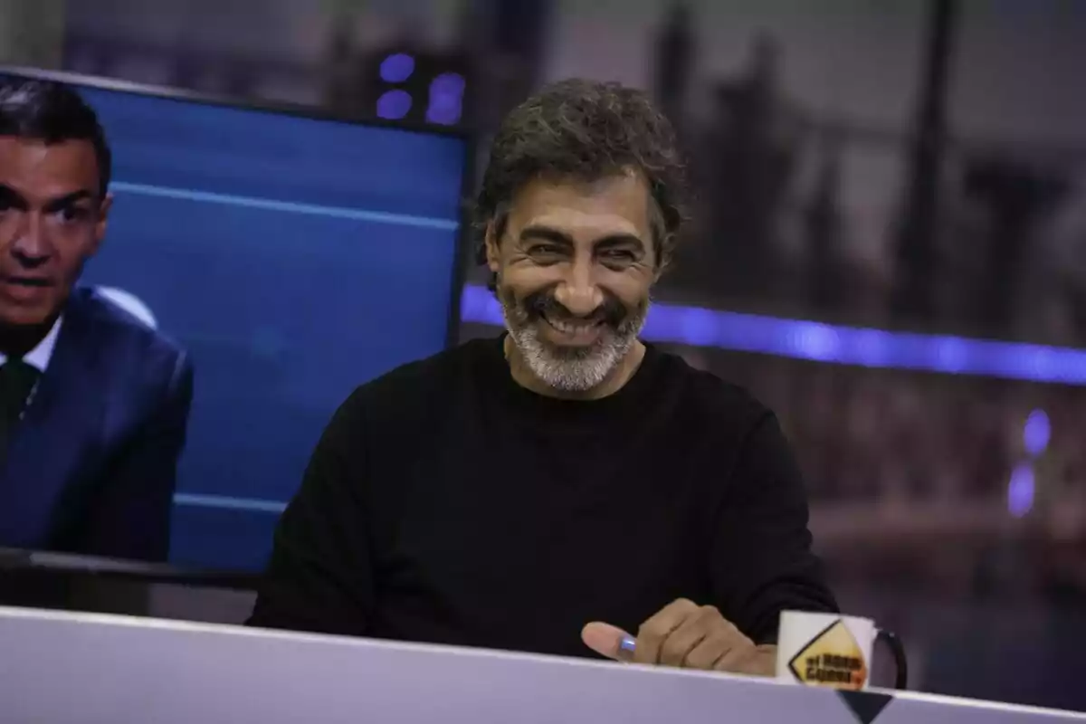 Juan del Val de cabell canós i barba somriu mentre està assegut a El Hormiguero amb una tassa i una pantalla al fons Juan del Val de cabell canós i barba somriu mentre està assegut a El Hormiguero amb una tassa i una pantalla al fons