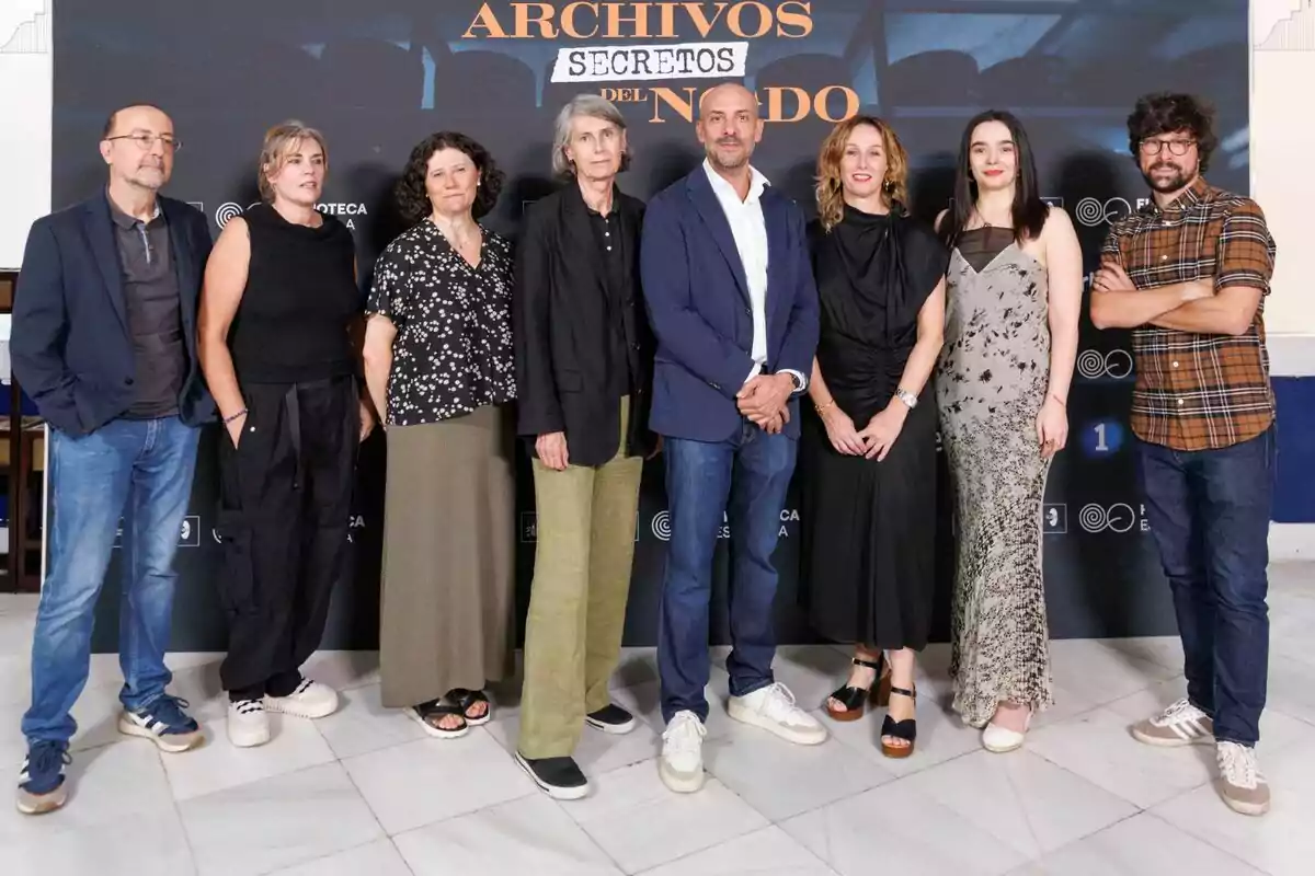 Ocho personas posan de pie frente a un fondo promocional de un evento llamado Archivos Secretos del NODO Ocho personas posan de pie frente a un fondo promocional de un evento llamado Archivos Secretos del NODO