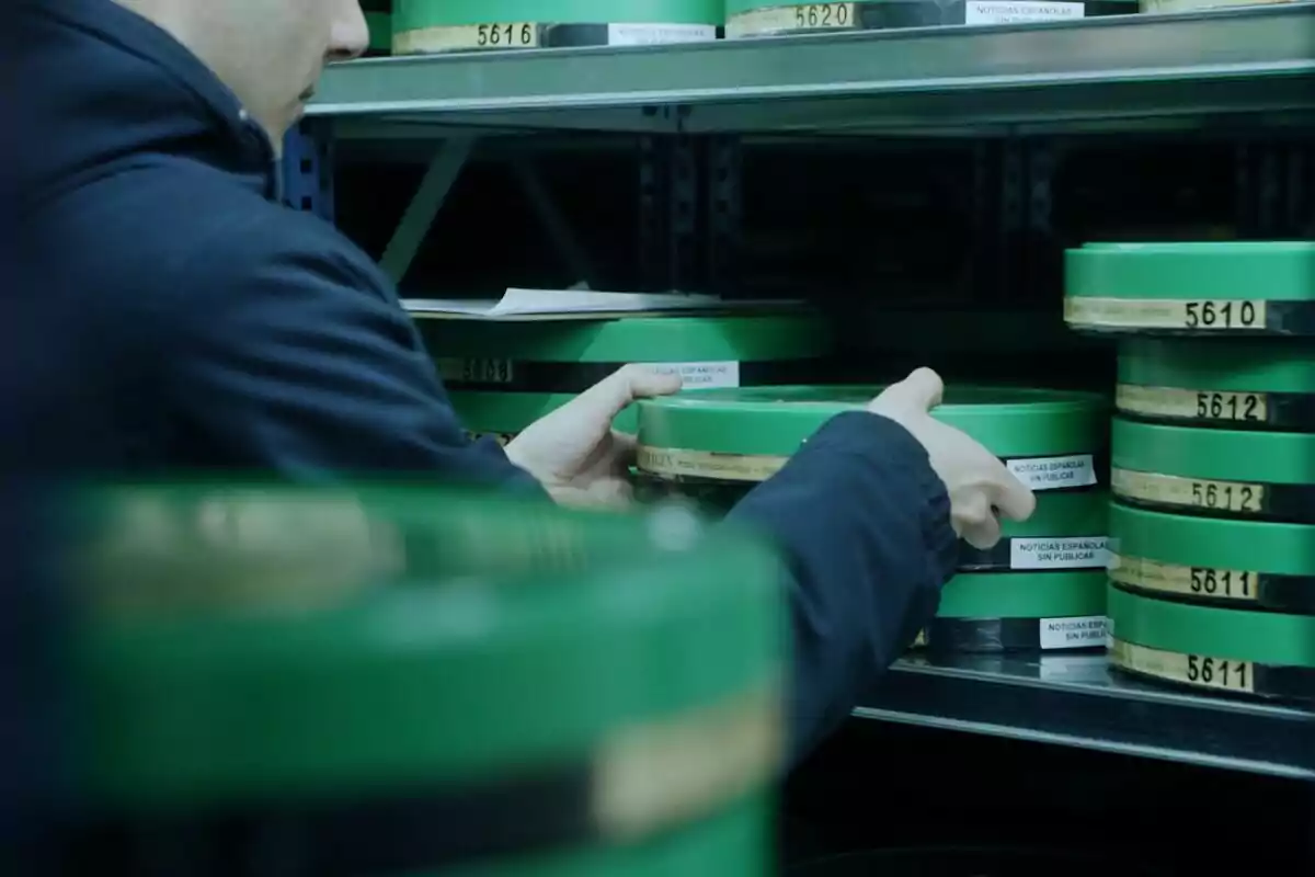 Persona acomodando latas verdes de películas en un estante de archivo en Los archivos secretos del NO-DO
