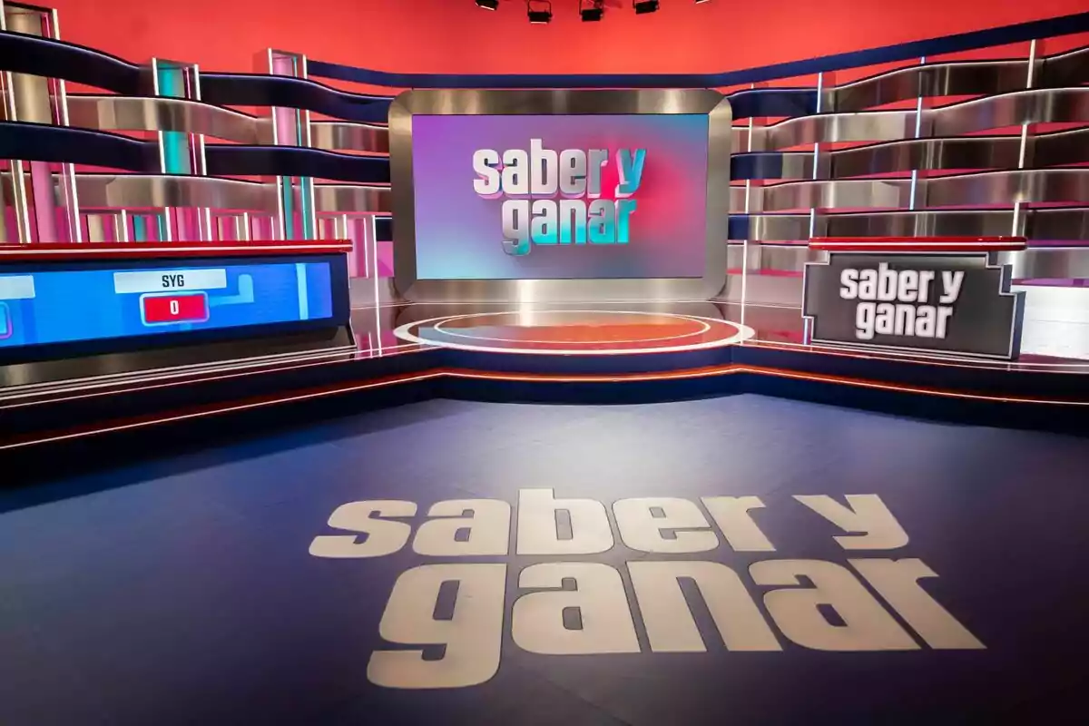 Plató colorit i modern del programa de televisió Saber i Guanyar amb el logotip visible a terra i en diverses pantalles Plató colorit i modern del programa de televisió Saber i Guanyar amb el logotip visible a terra i en diverses pantalles