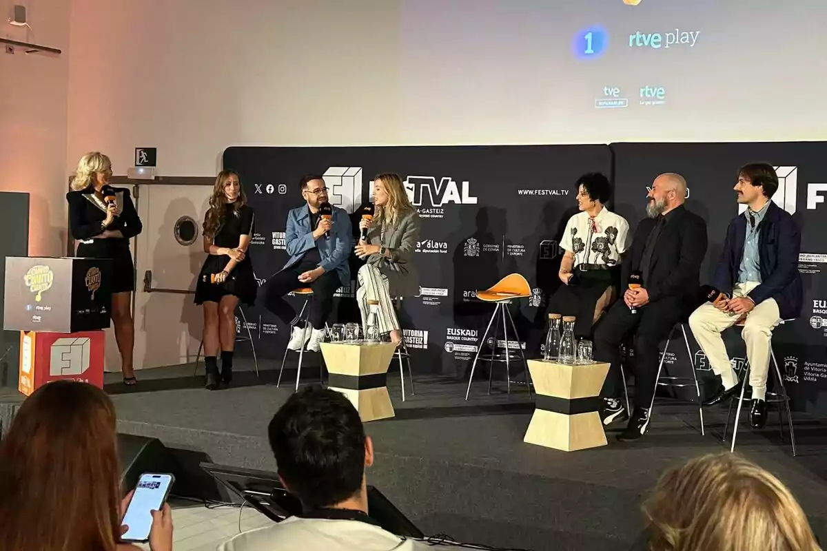 Un grupo de seis personas formado por María Eizaguirre, Eva Soriano, Aníbal Gómez, Miriam García Corrales y Ricardo Castella está sentado en un escenario participando en una charla o panel de Cuánto, cuánto, cuánto, mientras una mujer de pie sostiene un micrófono y modera el evento, con público observando y un fondo con logotipos de un festival y RTVE. Un grupo de seis personas formado por María Eizaguirre, Eva Soriano, Aníbal Gómez, Miriam García Corrales y Ricardo Castella está sentado en un escenario participando en una charla o panel de Cuánto, cuánto, cuánto, mientras una mujer de pie sostiene un micrófono y modera el evento, con público observando y un fondo con logotipos de un festival y RTVE.