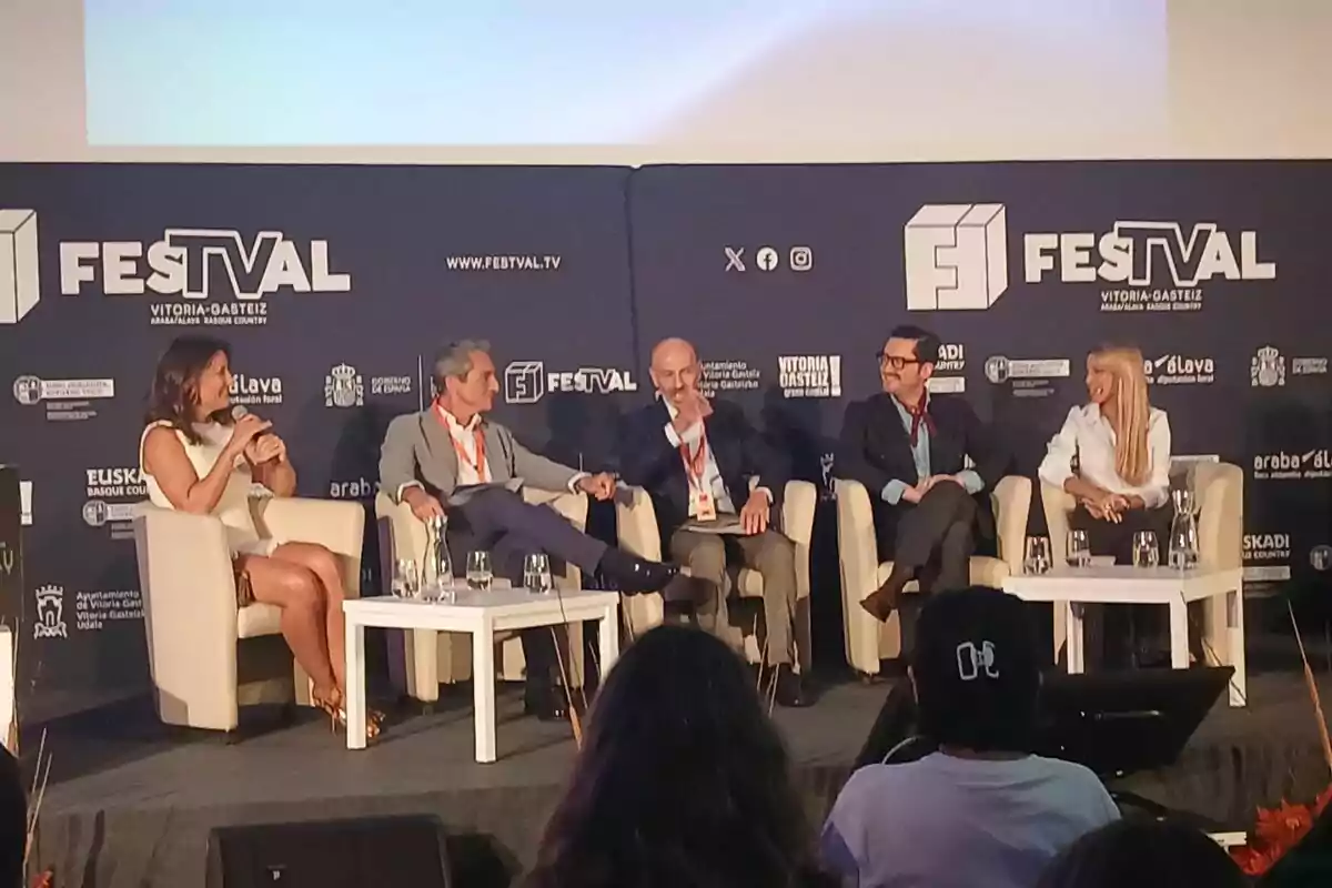 Nagore Robles, Juan Baixeras, Alberto Carullo, Sebastián Gallego i Oriana Marzoli asseguts en butaques blanques participen en una taula rodona en un escenari durant un esdeveniment anomenat FesTVal a Vitòria-Gasteiz, amb públic observant en primer pla.