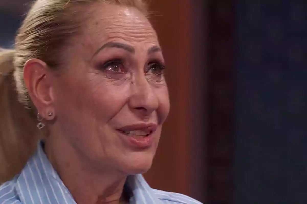 Rosa Benito de cabello rubio recogido con expresión emotiva y lágrimas en los ojos en MasterChef Celebrity, usando una camisa azul de rayas y aretes pequeños